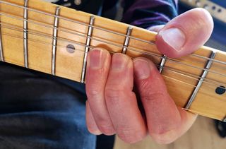 Closeup of three fingers on a fretboard, bending a note