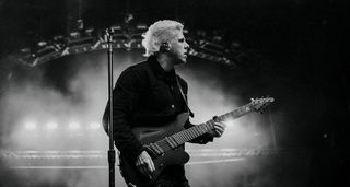 Mike String players his Aristides live onstage, in a black-and-white action shot with dry ice in the background