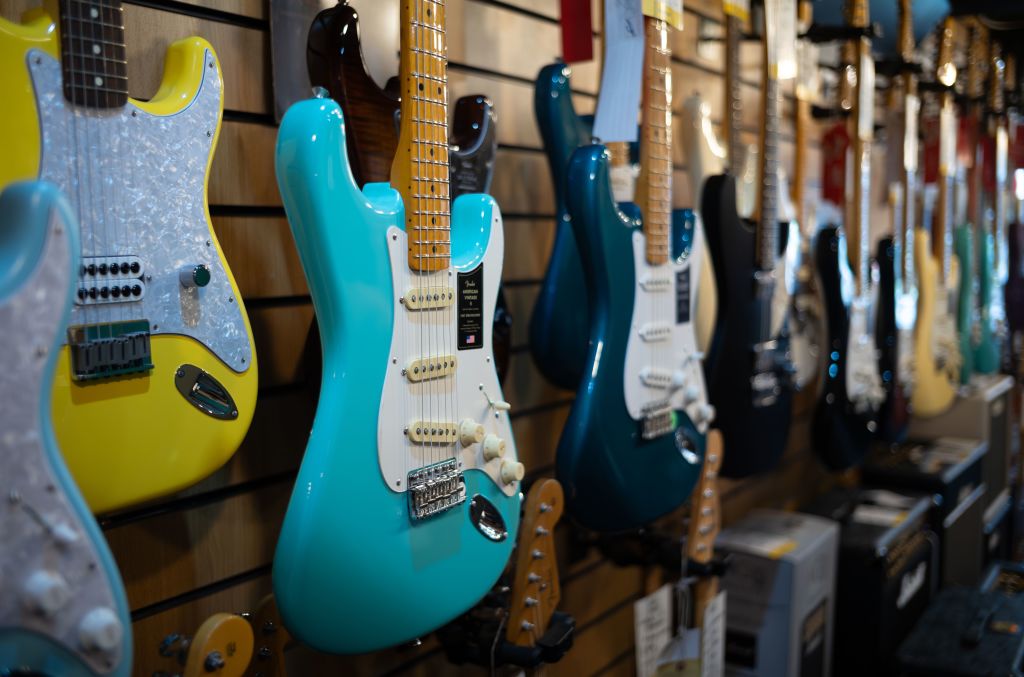 A turquoise Fender American Vintage II electric guitar hanging with other electric guitars for sale in Gak Music Emporium in Brighton, East Sussex, UK