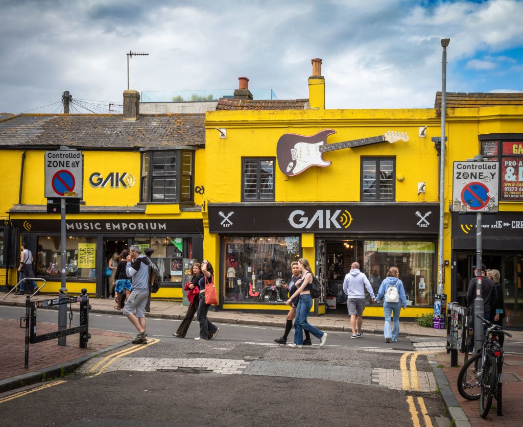 People walk past the yellow-painted Gak Music Emporium and guitar shop in The Lanes conservation area in Brighton, East Sussex, UK