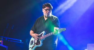 Will Sergeant of Echo & the Bunneymen plays a Daphne Blue Jazzmaster on a stage lit in blue-purple.