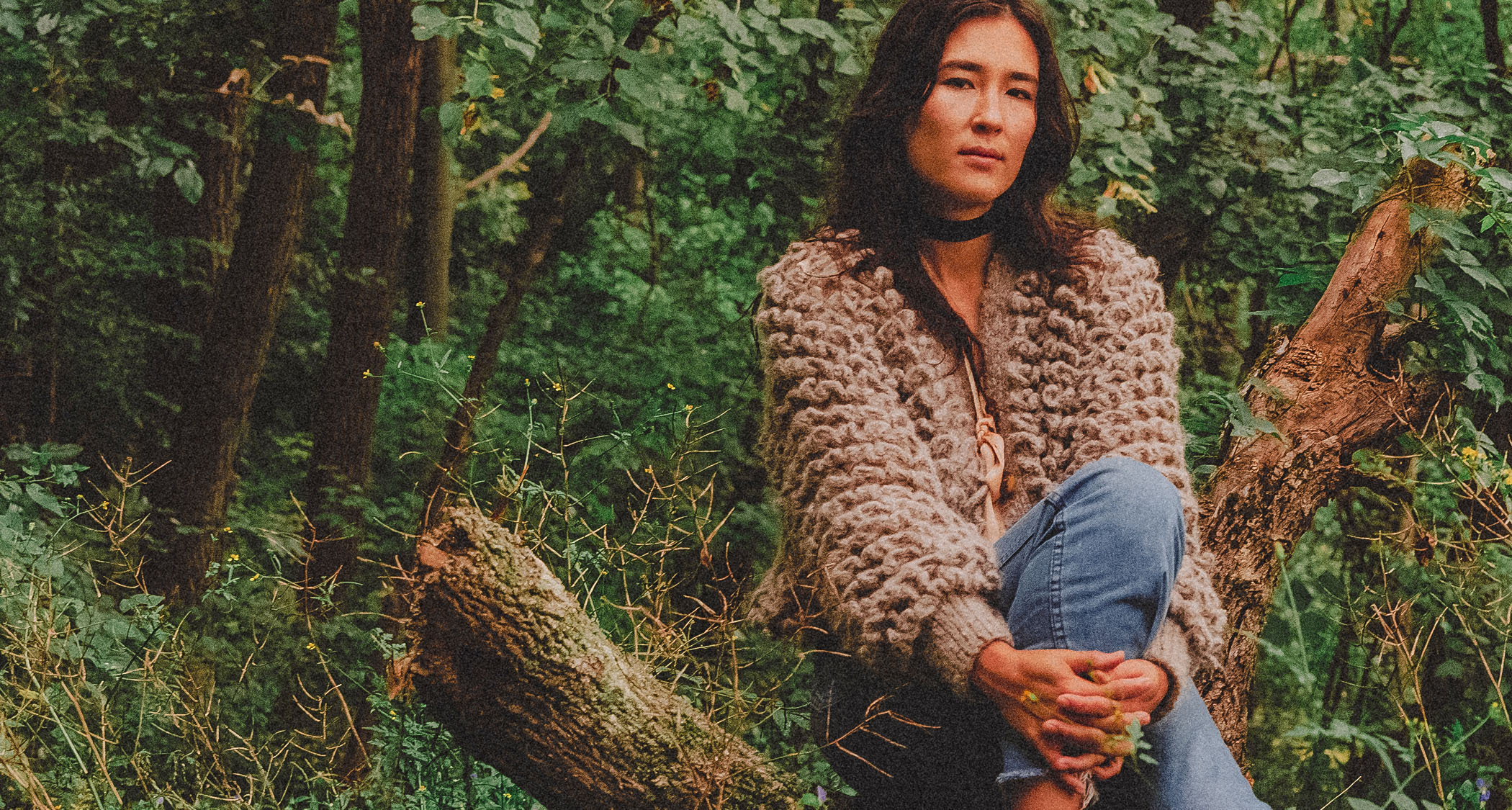 Lea Thomas sits on a log in the forest with her hands clasped round her leg.