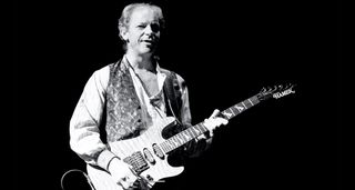 Martin Barre of Jethro Tull plays an HSS Hamer Superstrat (with a very highly figured maple top) in this black-and-white live shot from 1999. He wears a light shirt and a dark, patterned waistcoast.