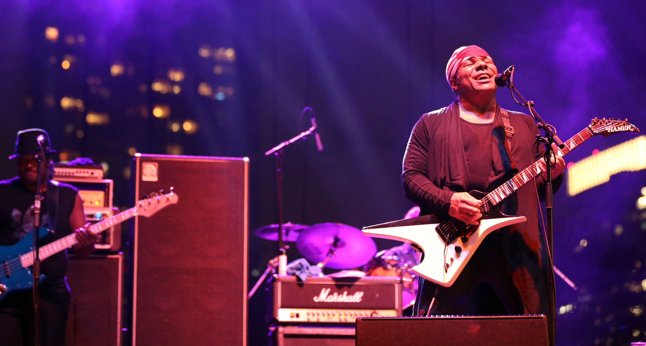 Dez Dickerson wears a red bandana and plays a crazy shaped Hamer electric guitar onstage at a Prince tribute show in 2017