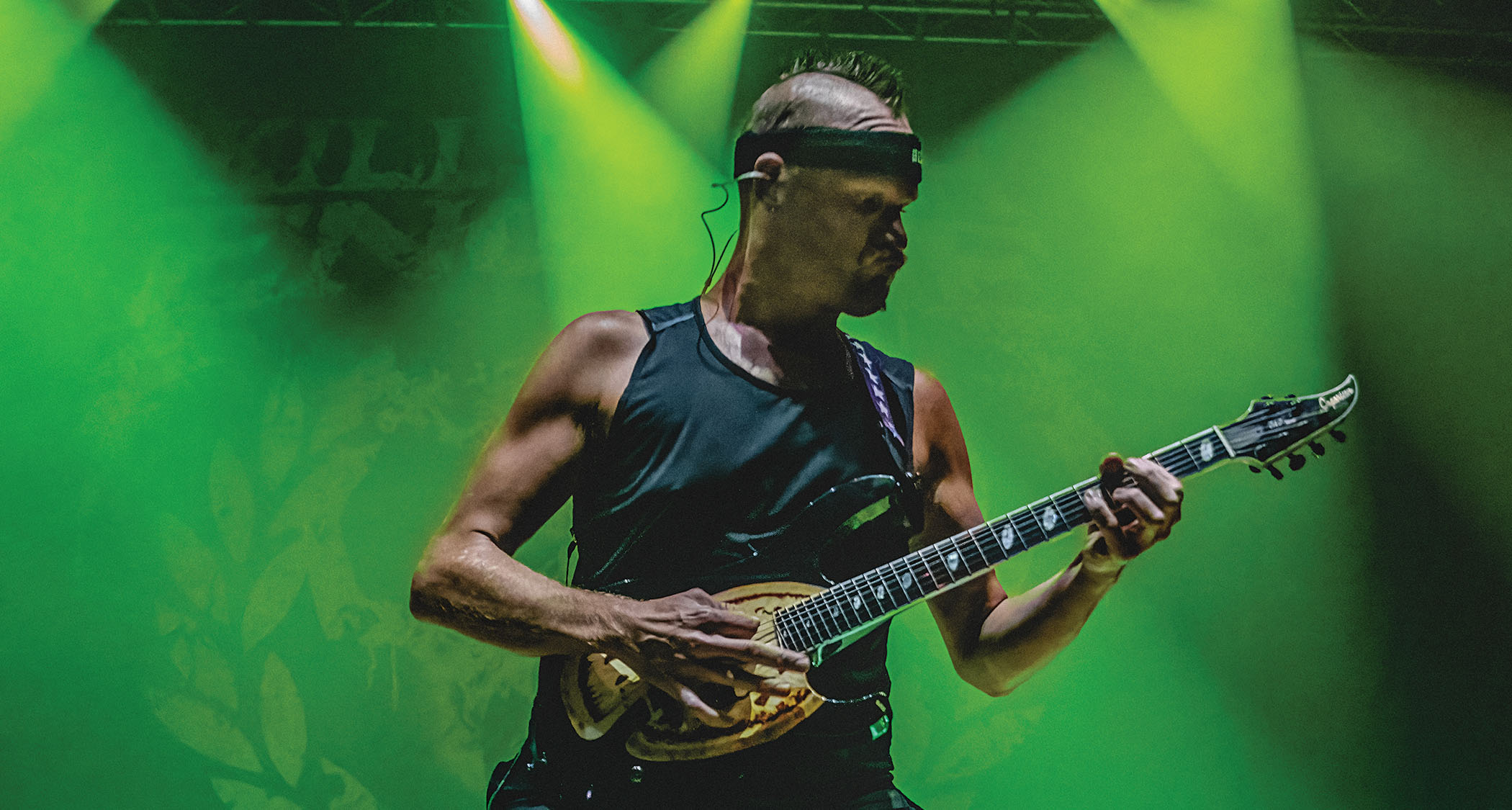 Adam Dutkiewicz of Killswitch Engage rocks a mohican and a Caparison on a stage bathed in green light.