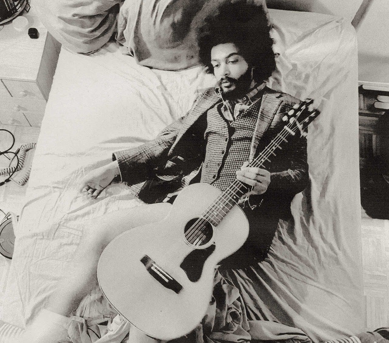 Yves Jarvis lies on a bed with an acoustic guitar