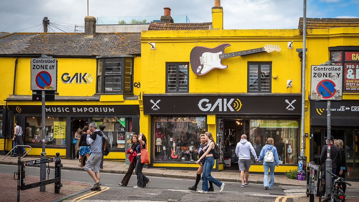 People walk past the yellow-painted Gak Music Emporium and guitar shop in The Lanes conservation area in Brighton, East Sussex, UK. 